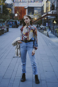 Full length portrait of young woman standing on footpath