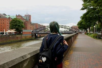 Rear view of woman walking by bridge over canal against sky in city