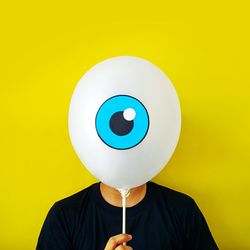 Man hiding face behind balloon against yellow background