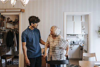 Smiling male healthcare worker talking to senior woman standing with walker at home