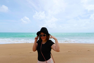 Woman wearing sunglasses standing at beach against sky