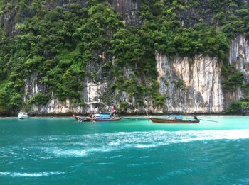 Longtail boats on sea against rock formation