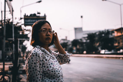 Youn woman looking away while standing against sky in city