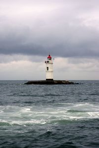 Lighthouse in sea against cloudy sky