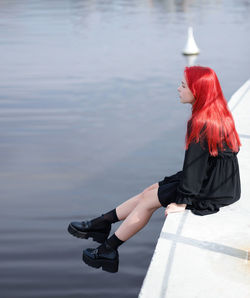 A young girl with red hair sits on the edge of a concrete platform above the water