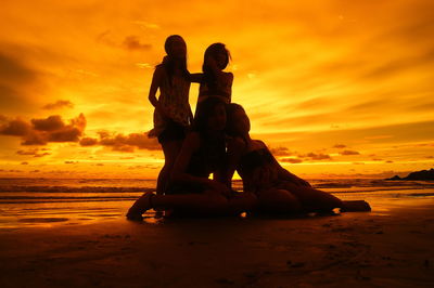 Friends sitting on shore against orange sunset sky
