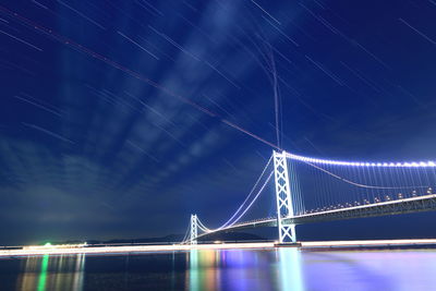 Illuminated akashi kaikyo bridge over sea against star trails