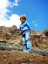 Full length portrait of boy standing on mountain against blue sky