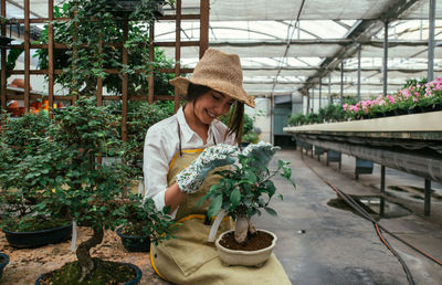 Woman sitting with plant in greenhouse