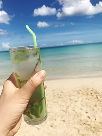 Cropped image of hand holding drink at beach against sky