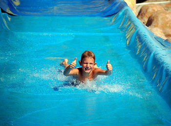 Portrait of happy boy showing thumbs up sign while sliding at water park