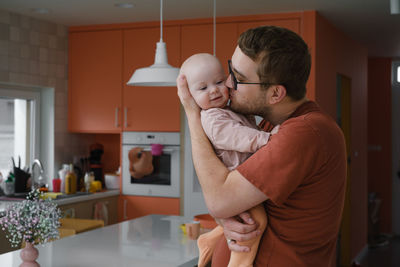 Daddy with baby girl in his hands cuddling on the kitchen at home, taking care of infant. father