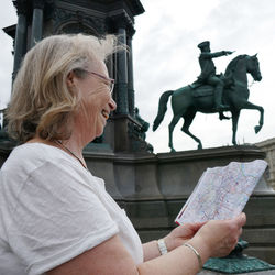 Smiling woman holding map while standing against statues