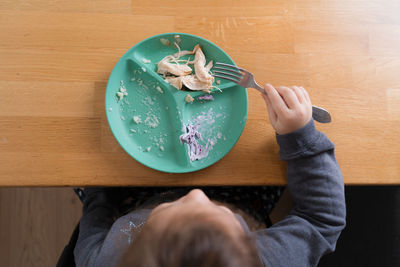 Little child girl sitting at the table and putting spoon at her mouth while eating porridge 