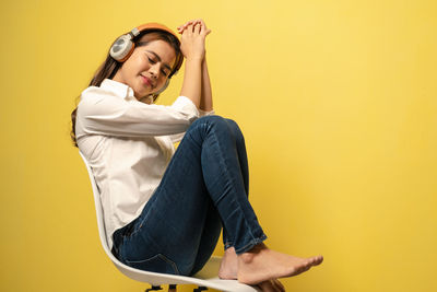 Young woman sitting against yellow wall