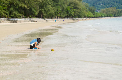 Teenage girl crouching on shore against sea at beach
