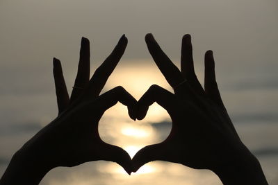 Close-up of hand holding heart shape against sky during sunset