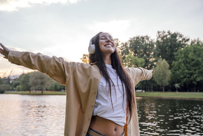 Woman with arms outstretched listening music by lake