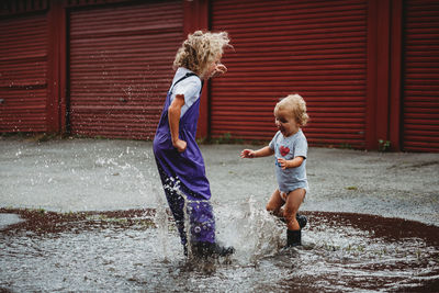 Girl and boy splashing in the water after the rain and laughing