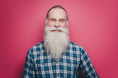 Portrait of smiling senior man with long white beard against pink background