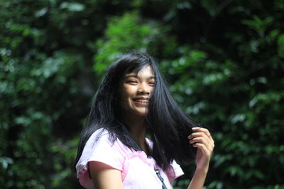 Smiling young woman looking away against trees