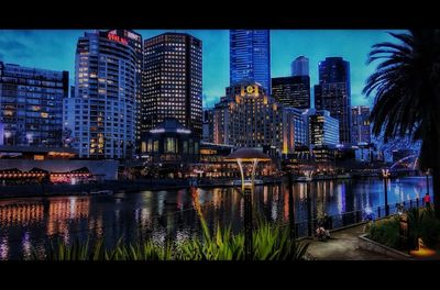 Illuminated buildings by river against sky in city