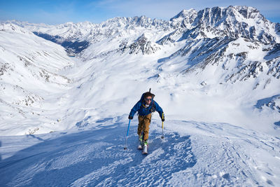 Man ski touring up slope with mountains behind him