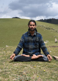 A indian young man practicing yoga in lotus pose, padmasana with gyan mudra in the mountain.