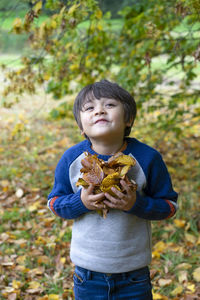 Portrait of smiling boy holding autumn leaves in park