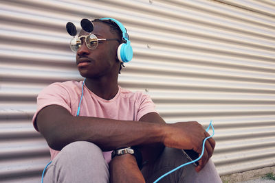 Man listening music while sitting against shutter