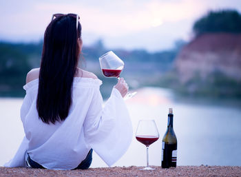 Rear view of woman having red wine against lake