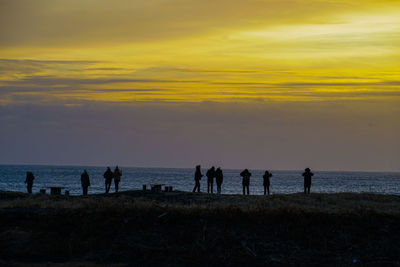 Silhouette people at beach against sky during sunset