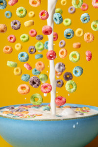 Dropping cereals and pouring milk into a blue bowl, on an orange background. preparing breakfast.