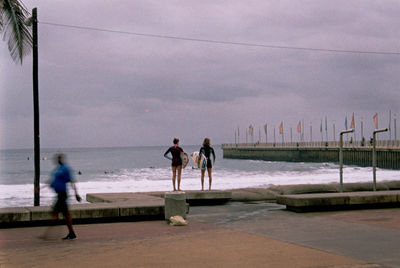 People walking on beach by sea against sky