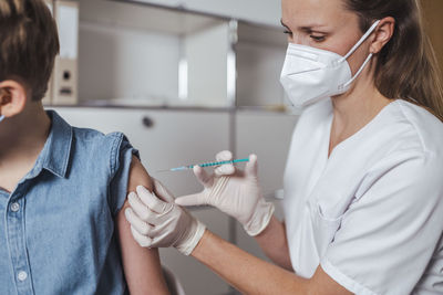 Healthcare worker in face mask administering boy with covid-19 vaccine