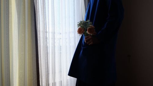 Woman holding umbrella standing by window at home