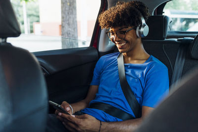 Smiling young man wearing wireless headphones texting through smart phone