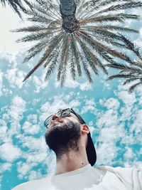 Low angle view of bearded man and palm trees against cloudy sky
