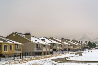 Snow covered houses by buildings against sky