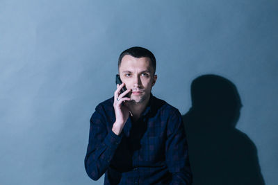 Portrait of man talking on mobile phone against wall