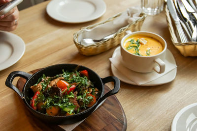 Black frying pan on a wooden plank served in a cafe, grilled meat with vegetables