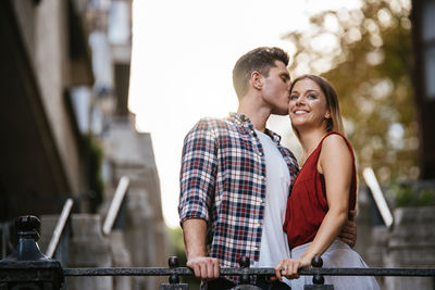 Low angle view of man kissing on woman forehead while standing outdoors