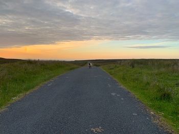 Road amidst field against sky during sunset