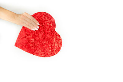 Close-up of hand holding red heart shape over white background