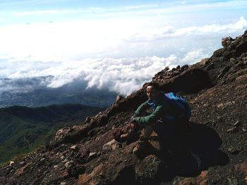 Man sitting on rock looking at mountains against sky