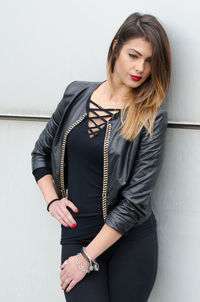 Beautiful young woman looking down while standing against wall