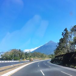 Road leading towards mountains against blue sky