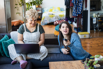 Young woman using phone while sitting on laptop