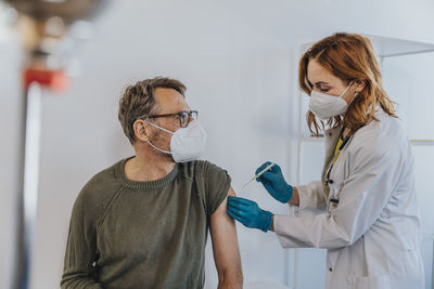 General practitioner injecting covid-19 vaccine in patient arm while standing at examination room