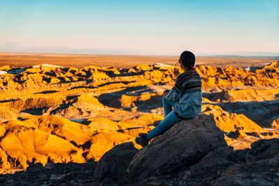 Woman sitting on rock at mountain against sky